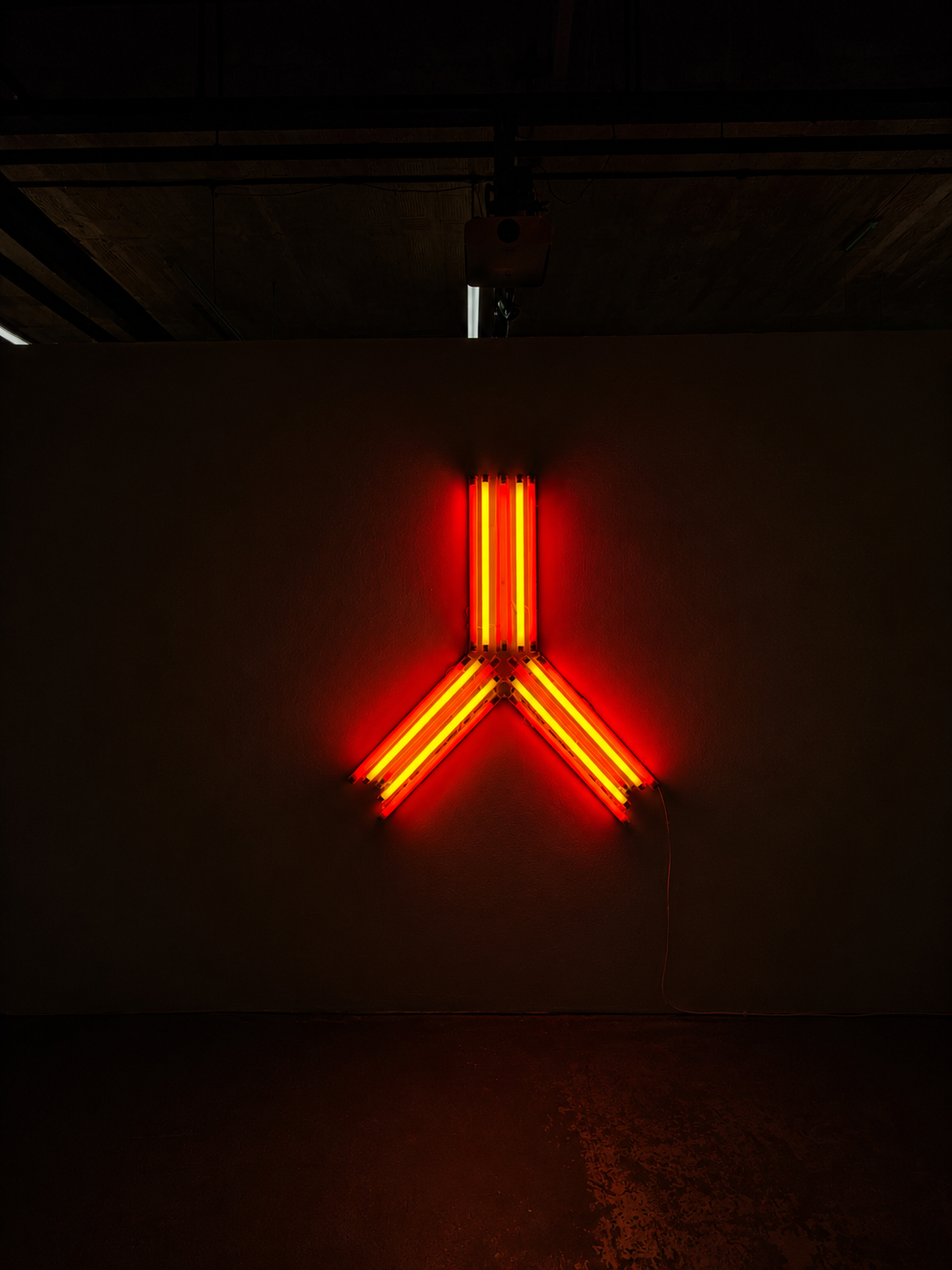 A fluorescent light installation of red and yellow alternating tubes in an upside down 'Y' shape