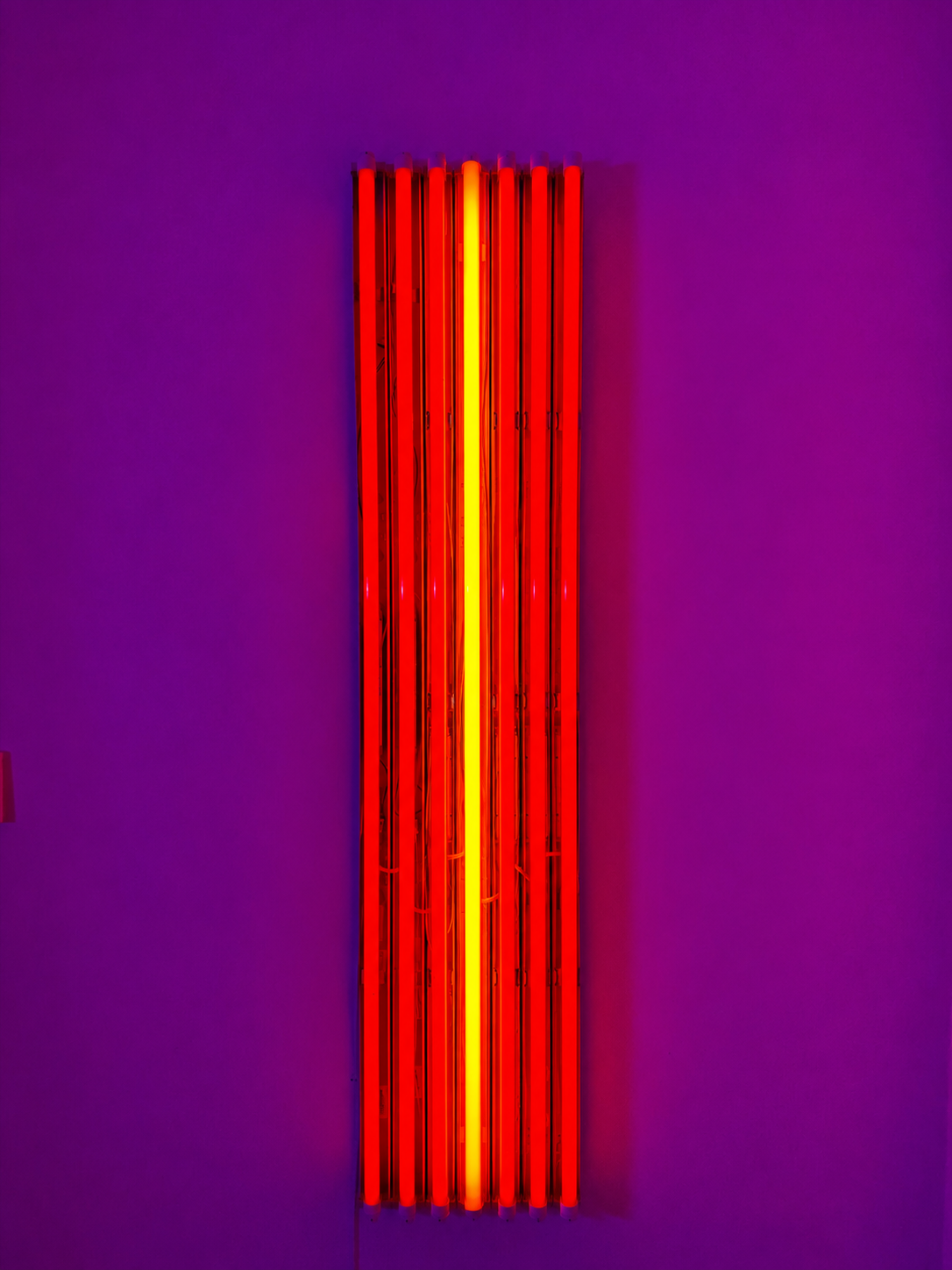 A row of fluorescent tubes in deep red, with an orange light in the centre