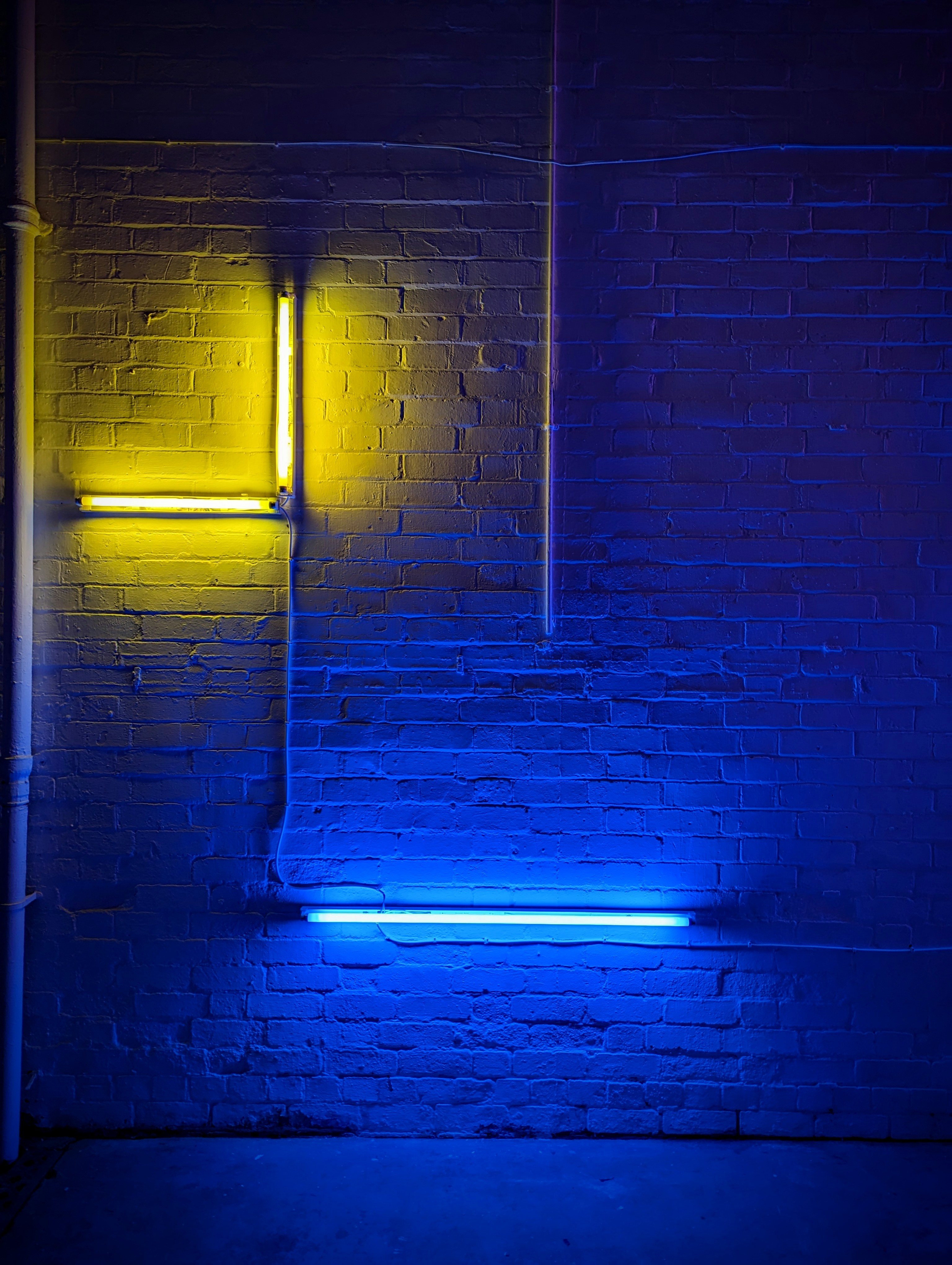 A blue and yellow fluorescent light installation against a brick wall