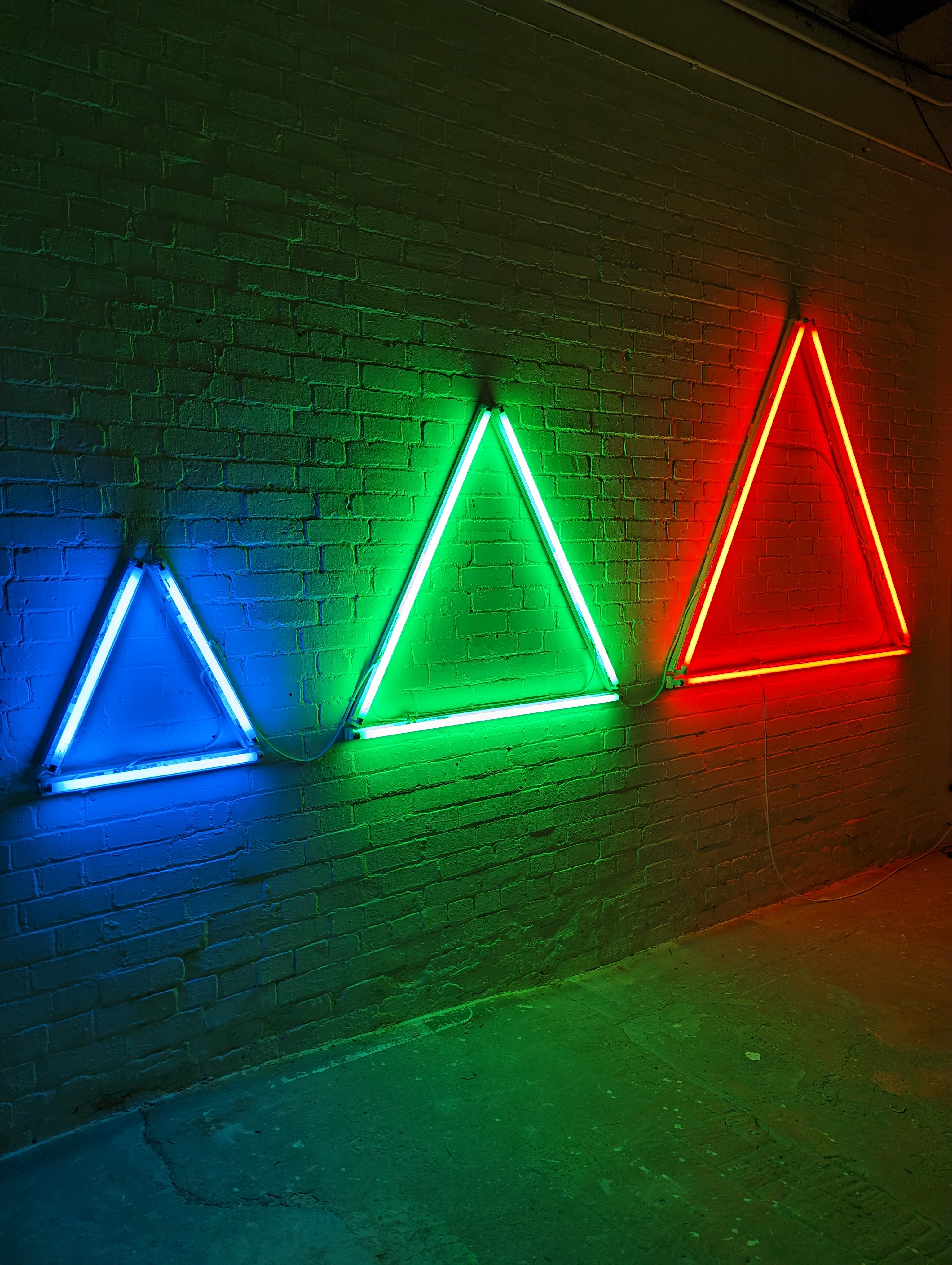 Three fluorescent triangles, one small and blue, one medium-sized and green, one large and red