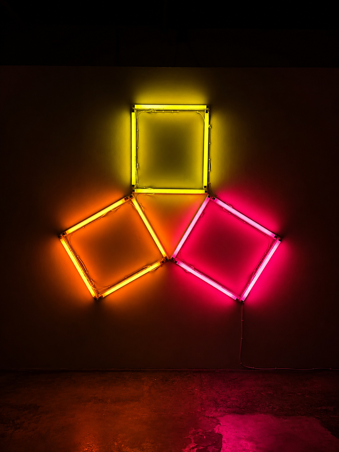 A fluorescent light installation of three squares, one orange, one yellow, one pink