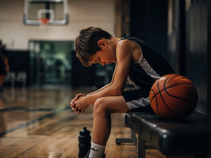 young athlete sitting on bench during game holding head down