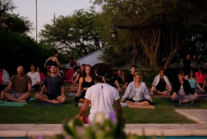 Clase de Yoga al aire libre. Profesor de espalda viendo a sus alumnos. Se ve la cara de algunos alumnos