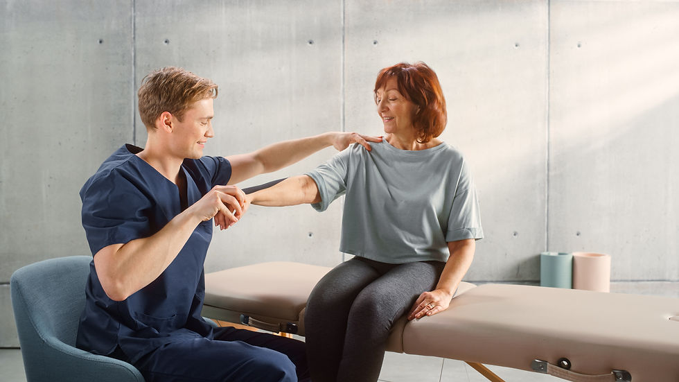 A physical therapist gently guides an older woman through a shoulder range-of-motion assessment while she sits on a treatment table in a bright therapy clinic.