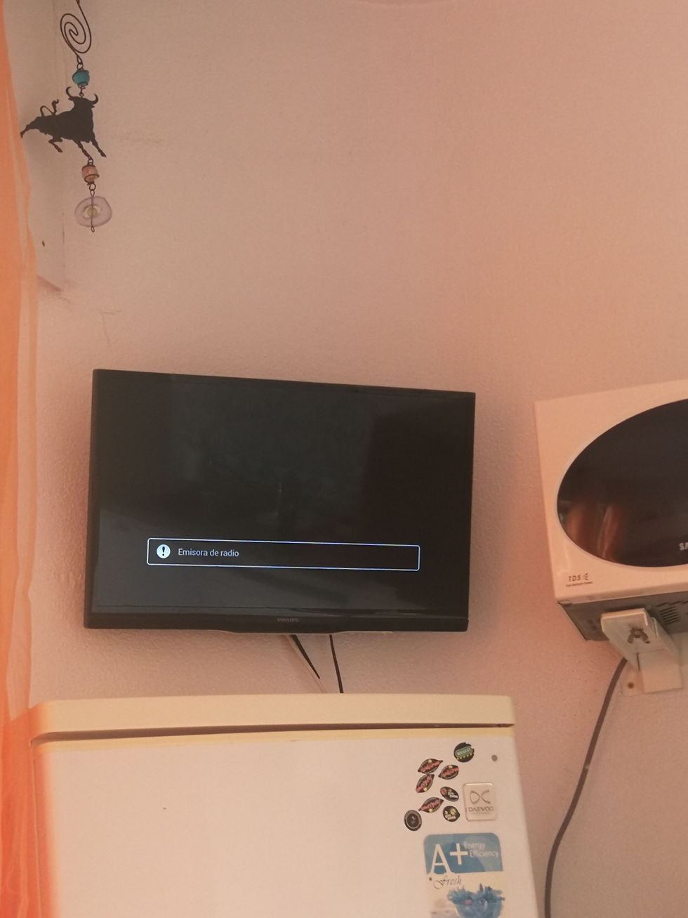 A small television, above a fridge and next to a microwave