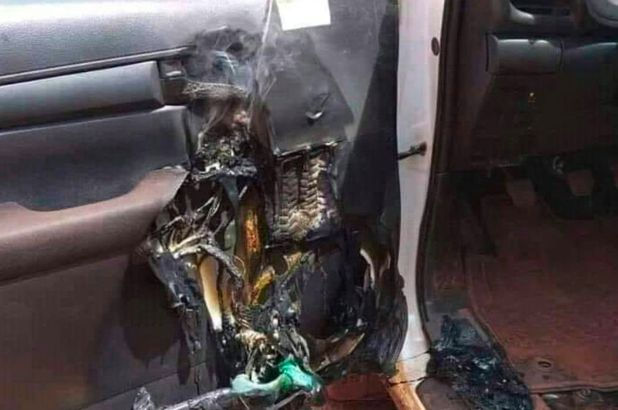 Car interior with a severely melted and burned door, showing damage and smoke. The mood is tense with visible charring and distortion.
