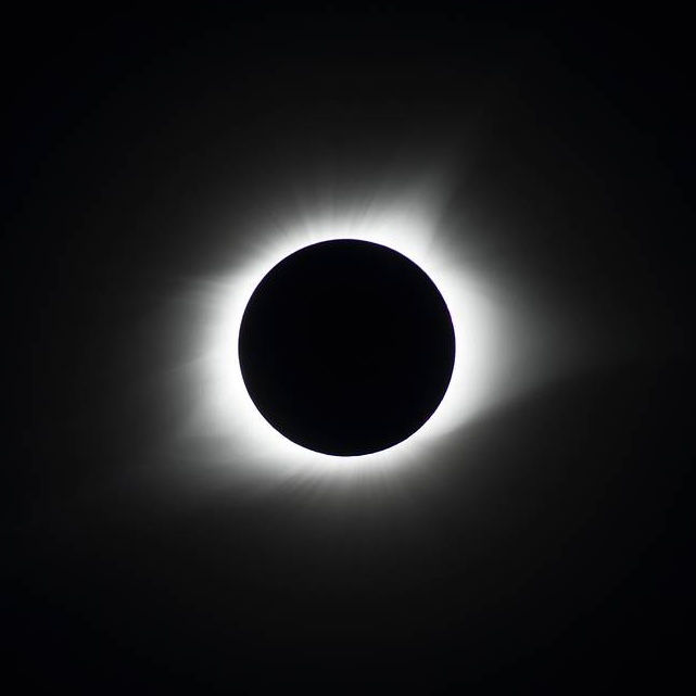 Solar eclipse with a dark moon obscuring the sun, halo of light visible. Black background emphasizes the glowing corona. Serene atmosphere.
