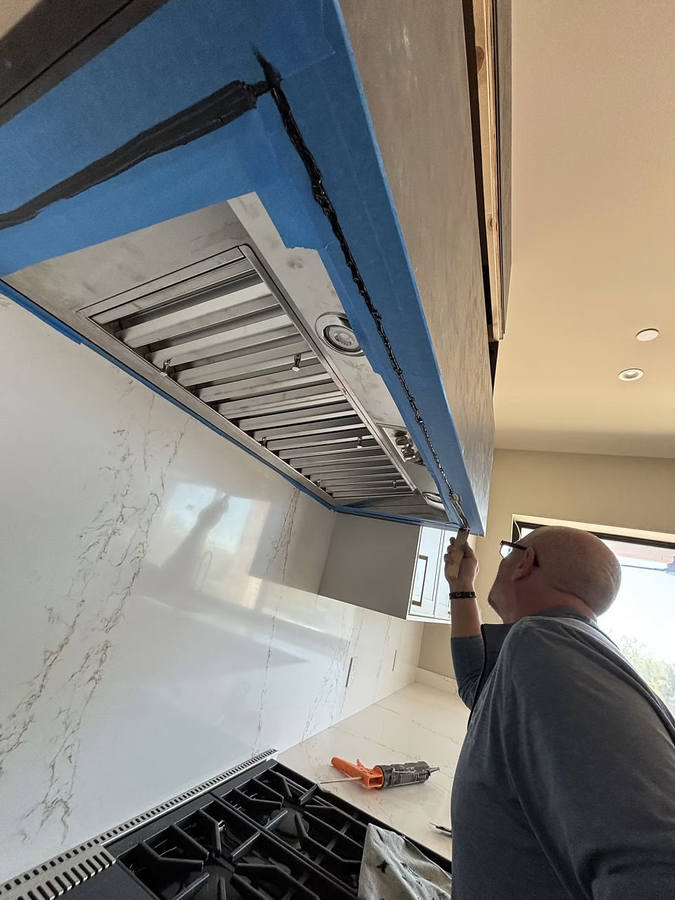Installer working at the range hood, showing how cabinetry, ventilation and construction must coordinate.