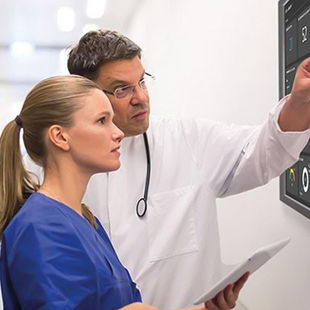 A male and female doctor in white coats looking at a digital display in a healthcare setting.