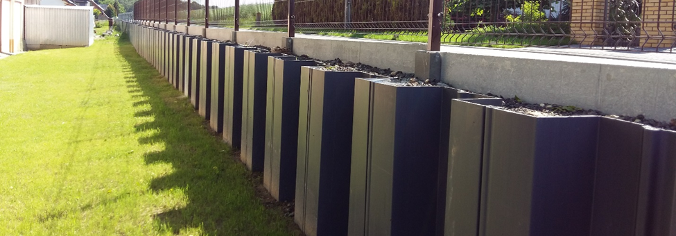 Residential retaining wall with striped vinyl sheet piles and fence, illustrating ESC USA‑made piles