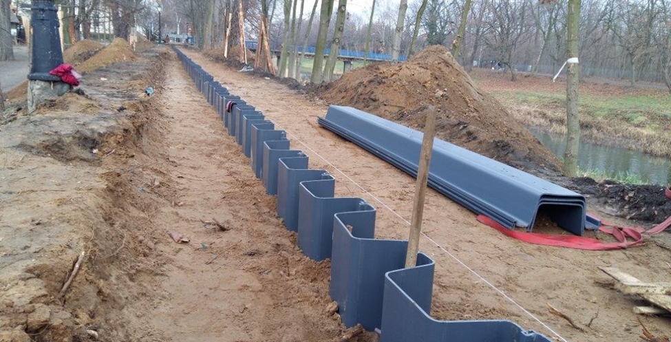 ESC vinyl sheet piles being installed in a trench near a waterway, demonstrating soil retention and erosion control applications