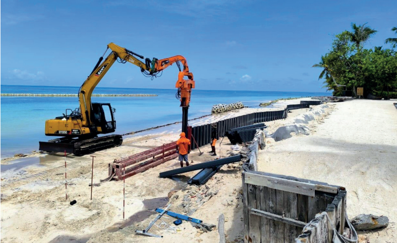Instalación de tablestacas de vinilo para protección costera mediante equipo de hincado en una zona de playa.