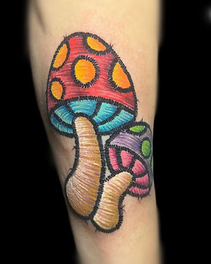 Colorful embroidered-style mushroom tattoo featuring bold stitching details. Inked by a talented tattoo artist in Lubbock. Get unique and creative designs at the best tattoo shop in Lubbock.