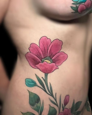 Vibrant floral tattoo on a person’s side, featuring a bold pink flower with green leaves. Expertly inked by a skilled tattoo artist in Lubbock. Visit the best tattoo shop in Lubbock for stunning custom designs.
