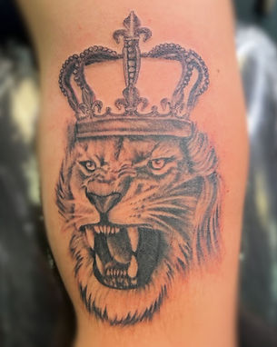 A detailed and striking black and grey lion tattoo wearing a regal crown, showcasing the exceptional skill of a tattoo artist at one of the best tattoo shops in Lubbock.