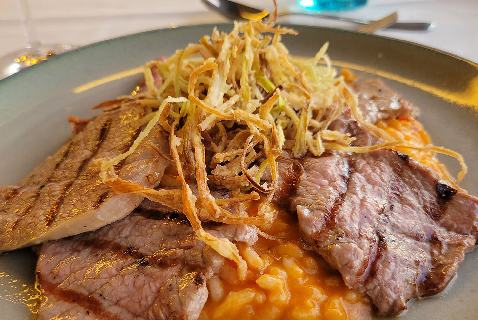 A dinner plate topped with rice in a savory red sauce and covered with slices of meat and fried onion slivers.
