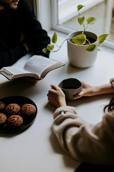 A man and a woman drinking coffee, reading a book and a bowl of muffins by Priscilla-du-Preez from Unsplash.