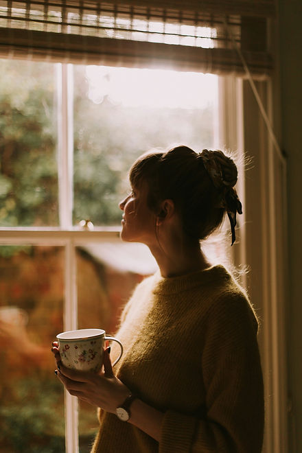 Photo of woman looking by the window and drinking coffee by Daiga-Ellaby from Unsplash.