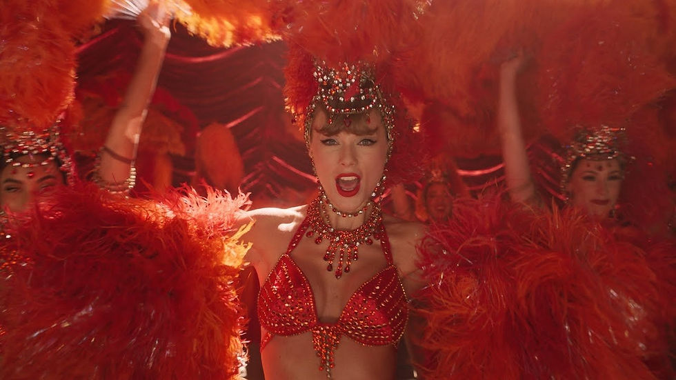 Performer in red sequined outfit, feathered headdress, and orange plumes dances energetically on stage, vibrant and lively setting.