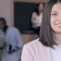 moving image of a women in professional attire smiling, with colleagues relaxing in the background