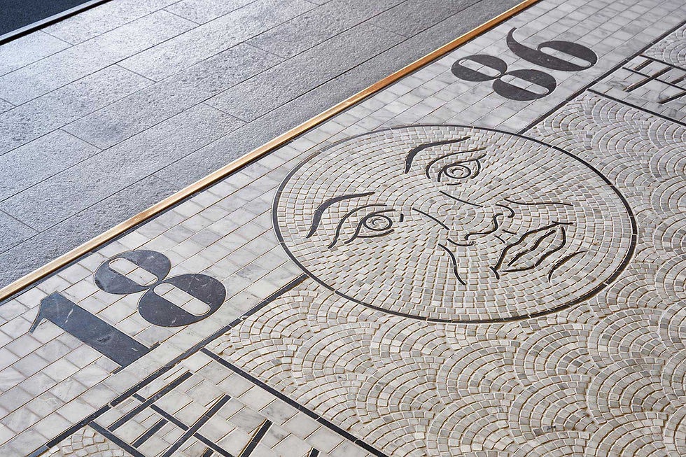Mosaic floor art with face pattern, and arch fan designs. Features gray tiles and a brass inset trim, creating an artistic urban atmosphere. A fully decorative mosaic logo.