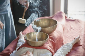 femme allongee sur table de massage reçoit soin aux bols chantants tibétain purification sauge