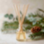 Homemade reed diffuser with Christmas pine and pine cone in the background
