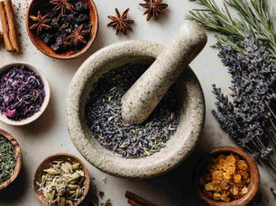 Flat lay of a mortar and pestle with small amount of crushed dried herbs (lavender, rose petals, rosemary) on a clean, modern white background. Nearby, small bowls with whole herbs, star anise, cinnamon sticks, and loose resins (like frankincense)