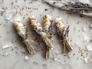 A clean, minimalist flat lay of handmade fire starters made from dried lavender sprigs and small cedar twigs dipped in melted wax. Each piece is lightly coated with natural soy or beeswax, with soft creamy tones and a slightly glossy finish. The lavender buds and cedar textures remain visible beneath the wax. Each bundle is neatly tied with a short cotton wick