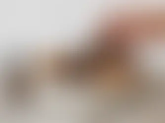 Hand legt een dennenappel in een keramieken schaal met gedroogde sinaasappel en kaneel naast een amberkleurig druppelflesje.