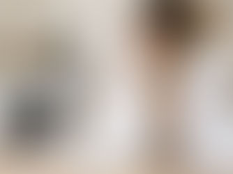Woman in a bright laundry room smells fresh white linens beside a washing machine and folded towels, looking content