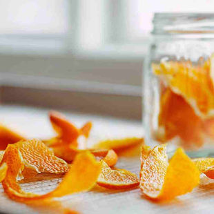 photograph of fresh orange peels drying on a white baking tray, thinly sliced citrus peels arranged loosely, a small clear glass jar partially filled with dried orange peel strips in the background.