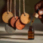 small terracotta discs hanging from twine, Show a small amber glass bottle with a dropper, in a hand applying essential oil onto the discs