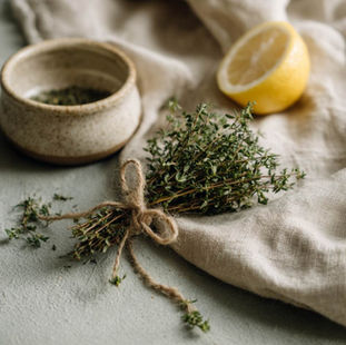 A loose bundle of fresh thyme tied with natural twine resting on aged linen, a few loose thyme sprigs scattered naturally beside it.