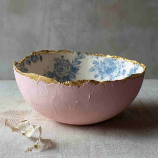 A handmade paper mâché bowl with a torn, organic rim and artisanal texture. The outside is painted in a rich "oud roze" (dusty pink) matte acrylic finish. The inside is lined with vintage-style floral toile paper in soft blues and whites, giving it a refined porcelain-like appearance. The rim is subtly accented with a delicate gold-painted edge for an elegant, handmade look. 