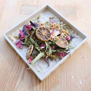 small concrete tray with potpourri ingredients such as dried flowers herbs and slice of lemon