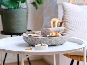 Minimalist white coffee table with a round stone incense burner releasing smoke, surrounded by natural décor in a cosy living room.