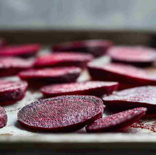 thinly sliced beetroot arranged on a metal baking tray, ready for oven drying. Deep ruby-red beet slices with visible texture and moisture, slightly overlapping