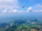 Paraglider flying over green landscape