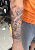 Tattooed arm with roses, clock, and text details. Artistic body art.