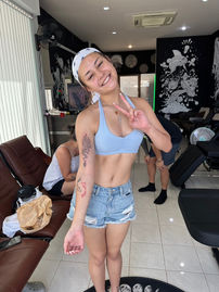 Smiling woman in blue top and denim shorts, tattoo, peace sign, portrait shot.