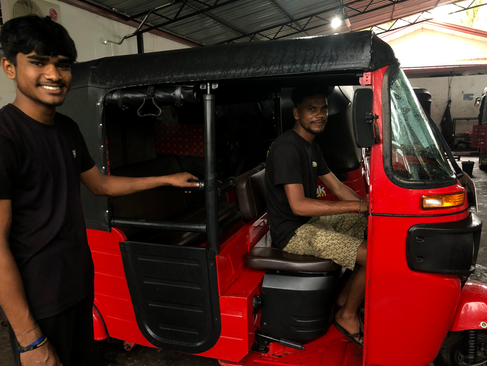 Two men smiling while fixing a tuk tuk at tuktuk rental's office