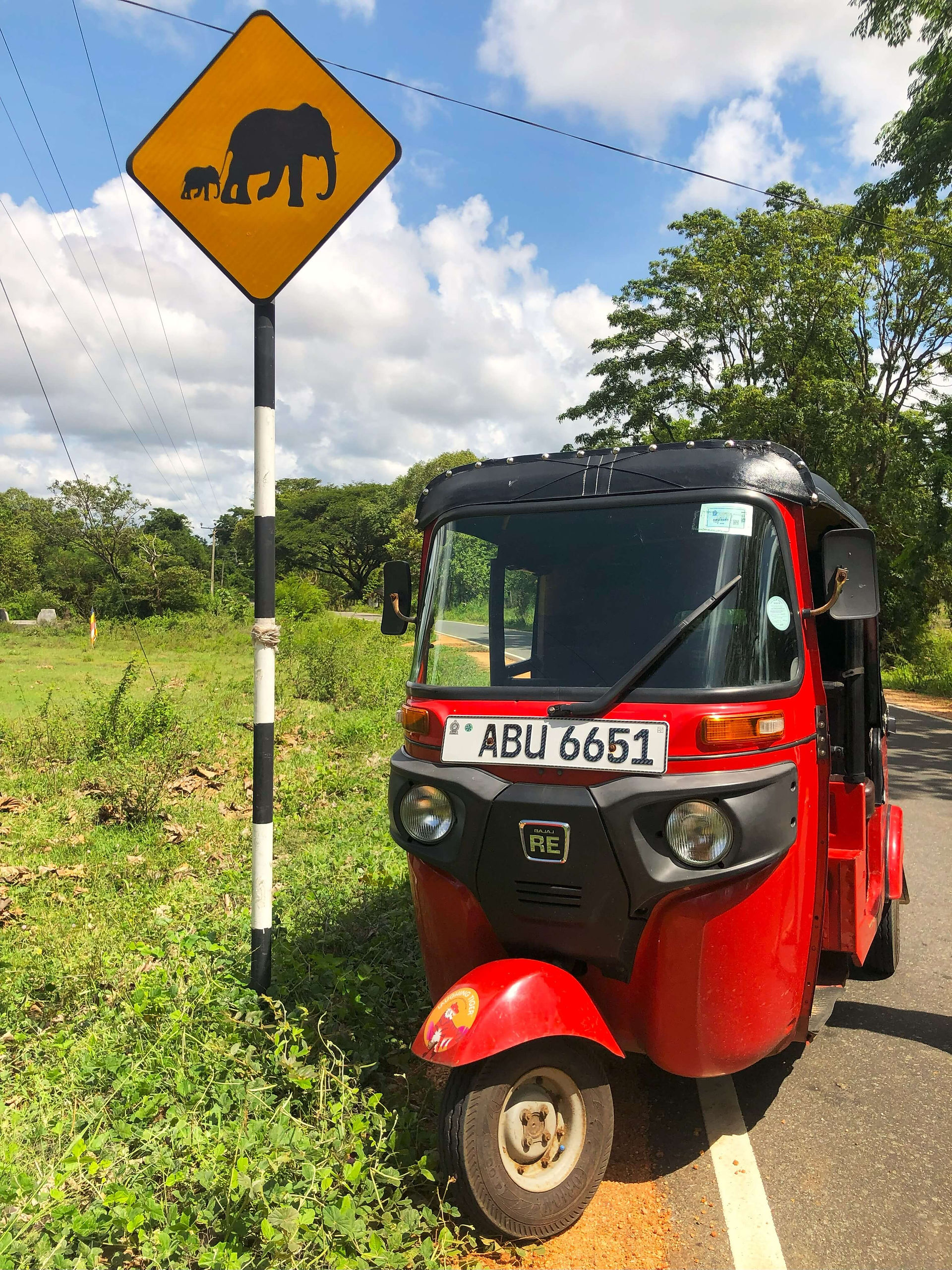 Red tuktuk next to a yellow elephant road sign