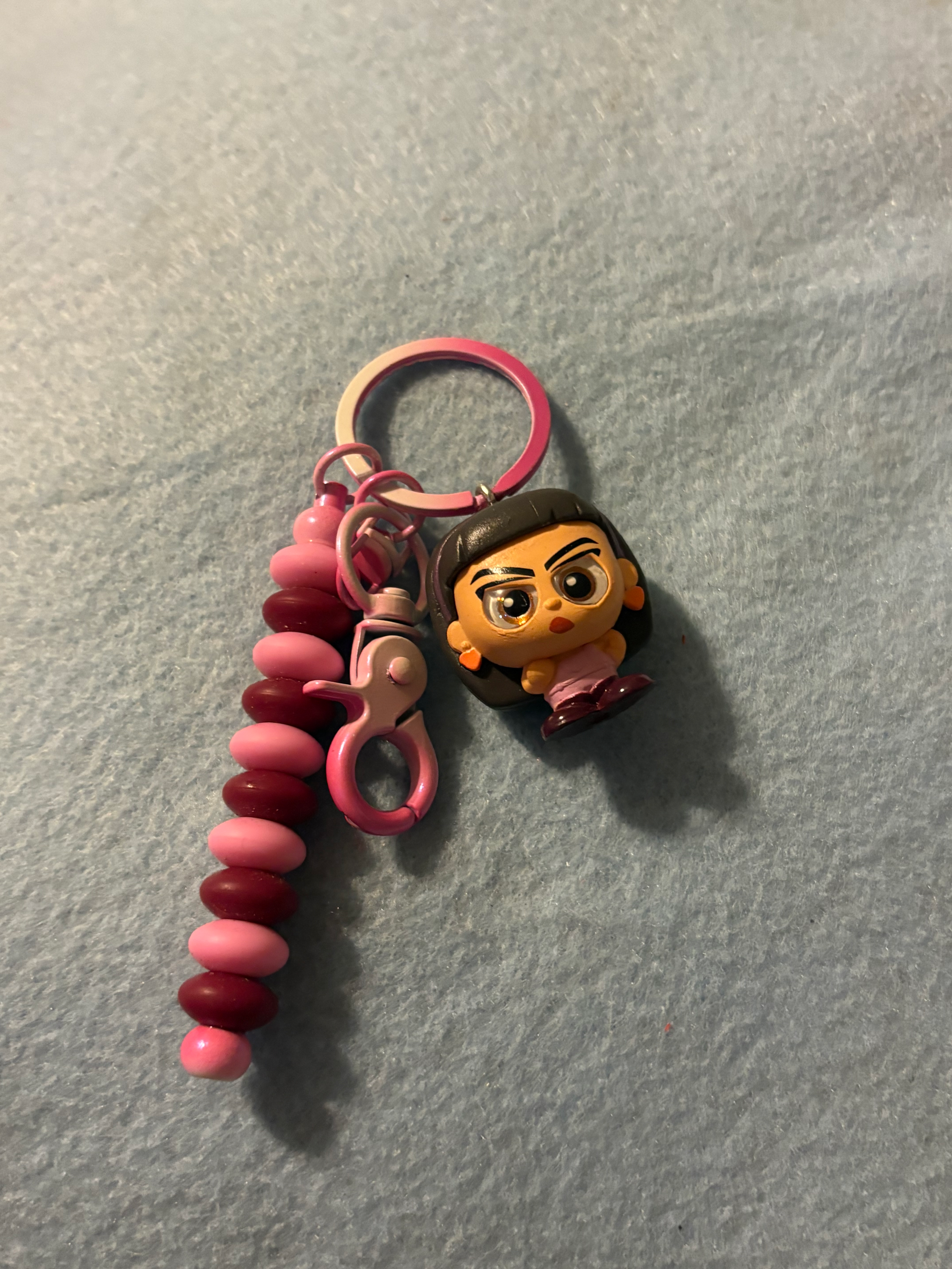 Keychain with Luisa Madrigal character charm and pink, maroon beaded dangle.