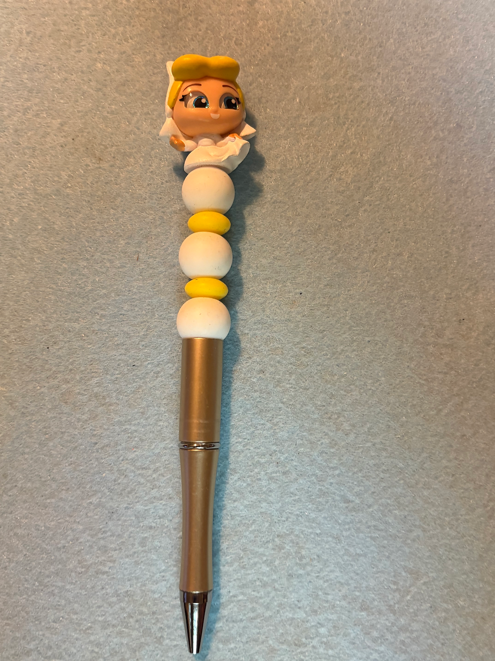 Thumbnail: Gold pen with a baby figurine and white yellow beads.
