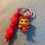 Thumbnail: Cute female character figure keychain with pink and red beads on blue.