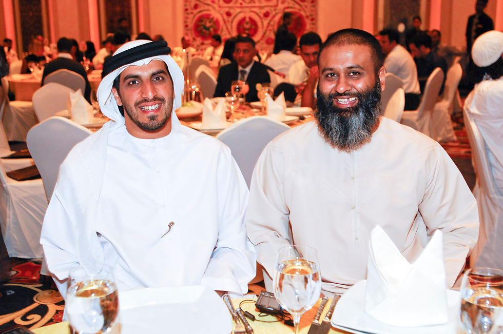 Two men in traditional attire smiling at a formal dinner.