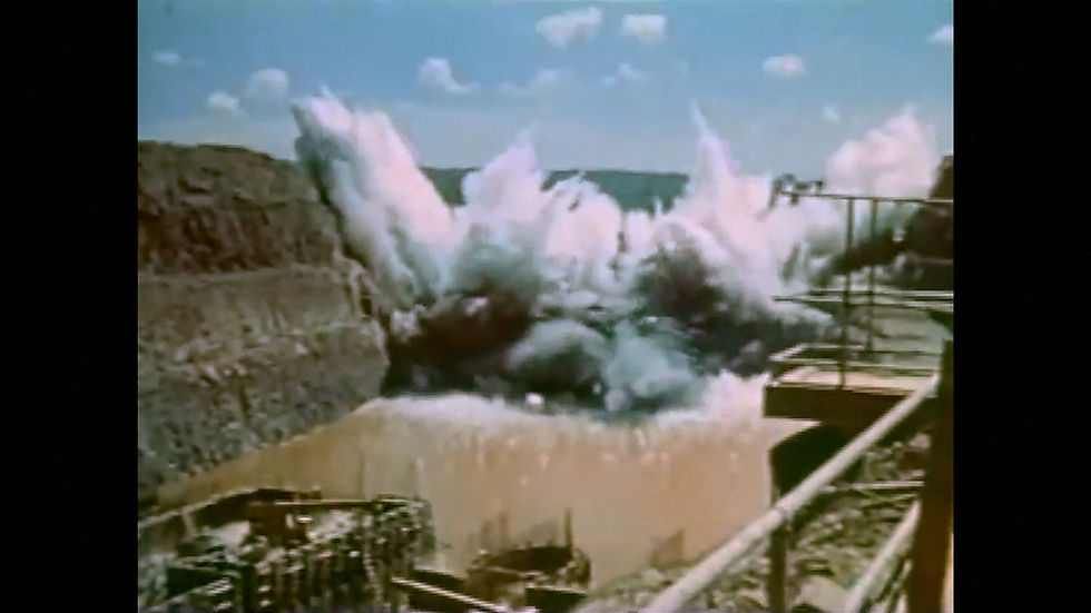 Cena do curta-metragem brasileiro Fronteriza (2025), de Rosa Caldeira e Nay Mendl, com o registro histórico da construção da Usina Hidrelétrica de Itaipu. Na imagem, há uma explosão dentro do curso de um rio já lamacento, em um vale cujas encostas já foram desbastadas e, no canto inferior esquerdo, estão embarcações de trabalho para a construção da barragem.