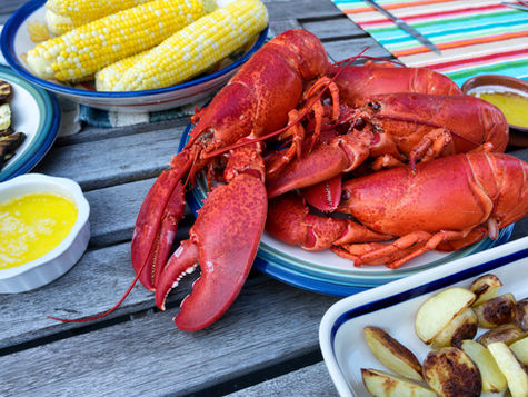 Steamed lobsters with drawn butter, corn and potatoes on a picnic table