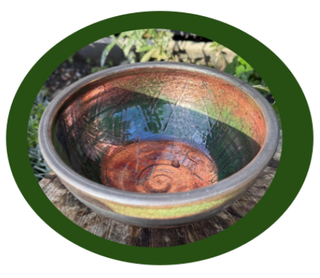 A ceramic bowl with red, green, and brown hues sits on a wooden surface outdoors, with greenery in
the blurred background.